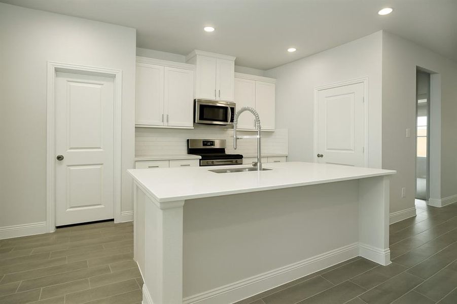 Kitchen with decorative backsplash, white cabinets, stainless steel appliances, recessed lighting, and a kitchen island with sink Kitchen with decorative backsplash, white cabinets, stainless steel appliances, recessed lighting, and a kitchen island with sink