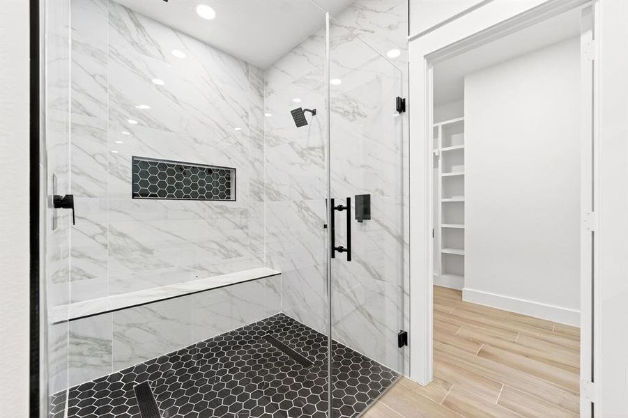 Spacious shower with large format marble-look tile, built-in bench, black hexagonal mosaic tile floor, and matte black fixtures Spacious shower with large format marble-look tile, built-in bench, black hexagonal mosaic tile floor, and matte black fixtures