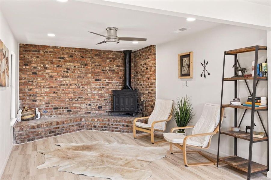 Living area featuring a wood stove, brick wall, ceiling fan, and light wood-type flooring