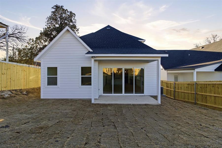 Rear view of house with a fenced backyard, roof with shingles, and a patio