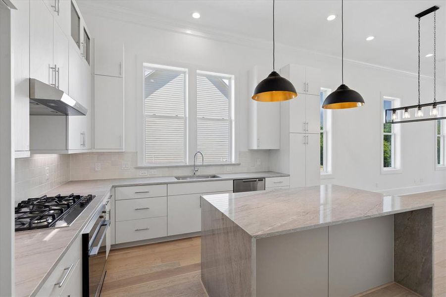 Open-concept kitchen featuring an oversized island with stone waterfall countertop, white shaker cabinetry, stainless steel appliances, and recessed lighting