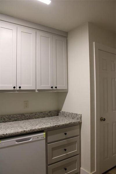 Kitchen featuring light stone counters, dishwashing machine, gray cabinetry, and white cabinetry