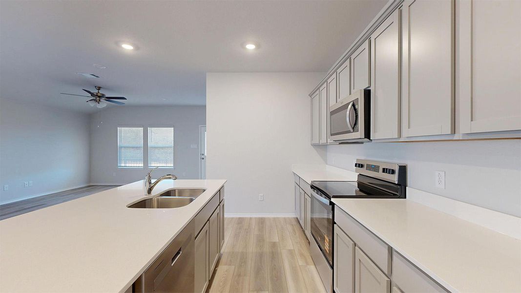 Modern kitchen featuring a spacious island with an undermount double-basin sink, light-colored countertops, stainless steel appliances, upper and lower cabinetry, and recessed lighting