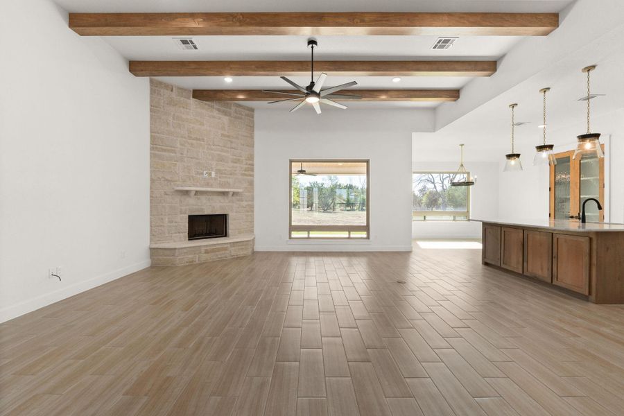 Unfurnished living room with wood finish floors, ceiling fan, a stone fireplace, and beam ceiling