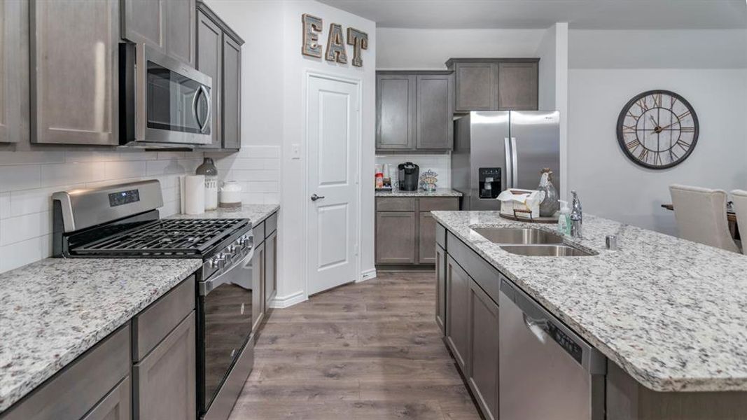 Kitchen featuring stainless steel appliances, dark wood-style flooring, light stone countertops, and tasteful backsplash Kitchen featuring stainless steel appliances, dark wood-style flooring, light stone countertops, and tasteful backsplash