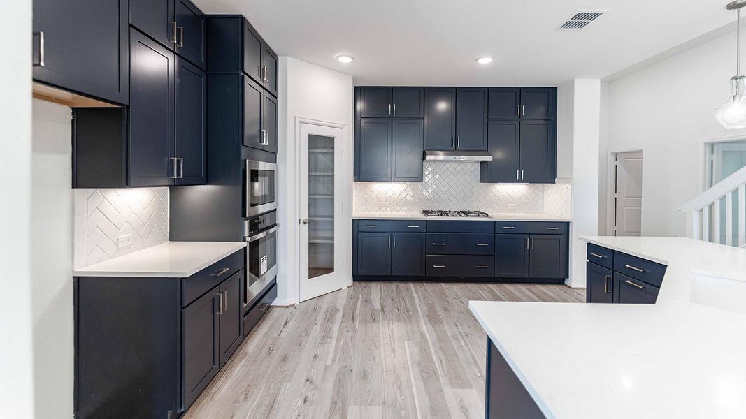 Kitchen featuring light stone counters, light wood-style floors, decorative light fixtures, stainless steel appliances, and decorative backsplash