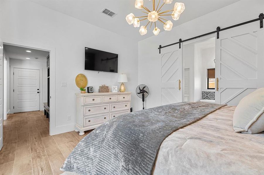 Bedroom featuring light wood-style flooring, a barn door, baseboards, visible vents, and a notable chandelier Bedroom featuring light wood-style flooring, a barn door, baseboards, visible vents, and a notable chandelier