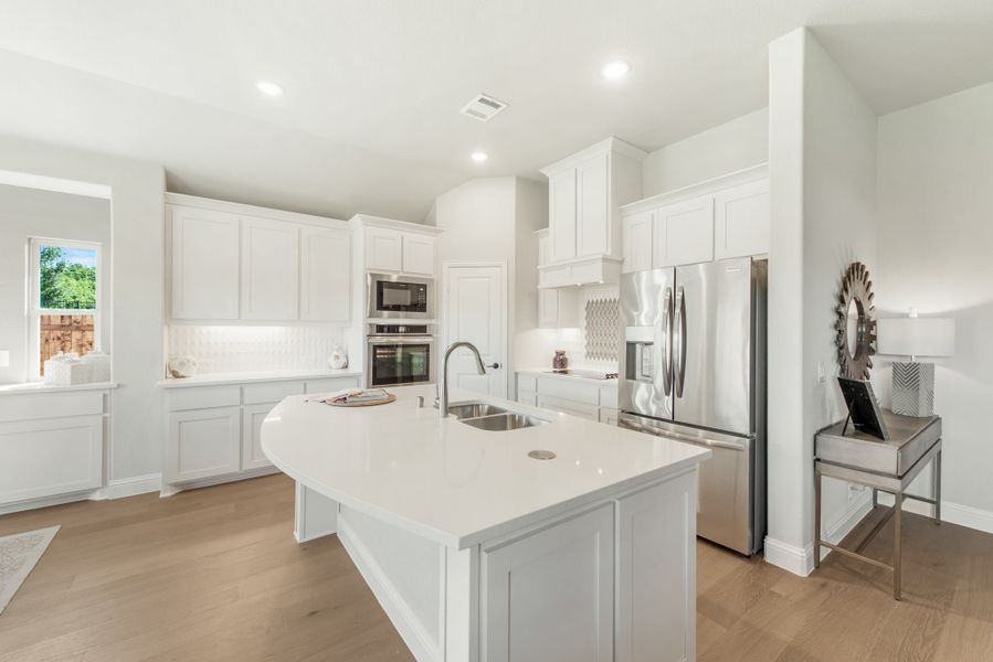Kitchen with white cabinets, large center island with sink, stainless steel appliances, and light hardwood floors