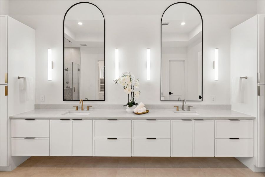 Spectacular double vanity spans the wall with generous countertop space, dual mirrors, and impressive vertical sconces that serve as both functional lighting and sculptural design elements. The luxurious vanity is flanked by two large linen closets on either side.