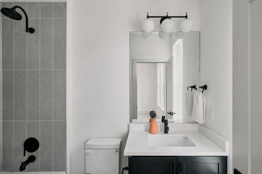 Bathroom featuring a tub and shower combination with gray vertical tile surround, matte black fixtures, a white vanity with an integrated sink, and a three-globe vanity light