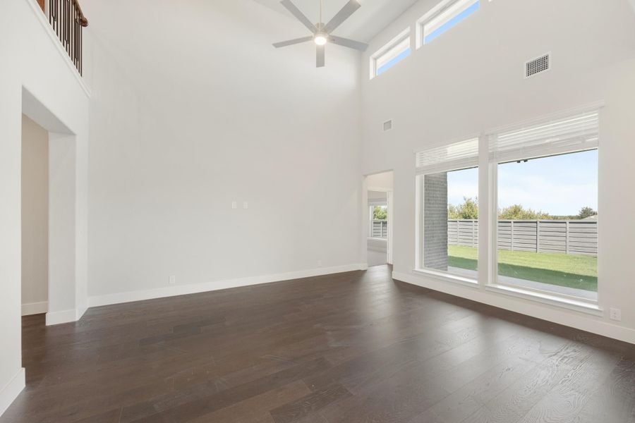 Open living room with two-story ceilings, dark hardwood floors, ceiling fan, and large windows overlooking backyard Open living room with two-story ceilings, dark hardwood floors, ceiling fan, and large windows overlooking backyard