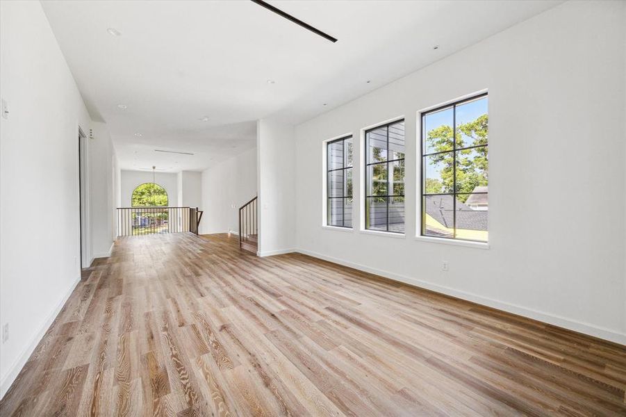 This expansive upstairs flex space can be a gameroom filled with natural light from the large windows. The wide, open space features rich wood flooring and leads to the library (oh the right), media room (to the left), additional secondary bedroom, utility room, and opens up to the grand entry below.