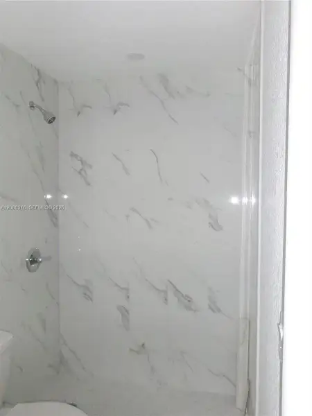 Shower enclosure featuring large-format veined tile surround, polished chrome shower head, and recessed ceiling lighting