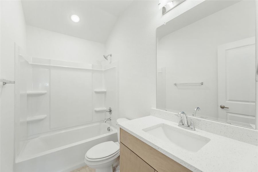 Full bathroom with white tub-shower combo, toilet, and single vanity with quartz countertop