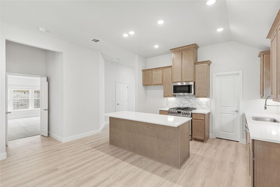 Kitchen with center island, tan wood cabinets, stainless steel appliances, and light wood floors Kitchen with center island, tan wood cabinets, stainless steel appliances, and light wood floors