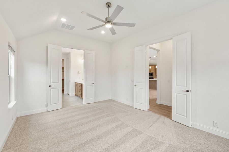 Empty master bedroom with carpet, ceiling fan, vaulted ceiling, and doors leading to bathroom and hallway