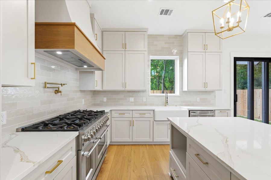 This stunning kitchen features a 48-inch FORNO gas range, custom vent hood, convenient pot filler, and thoughtfully designed built-ins for the microwave, trash bin, and more.