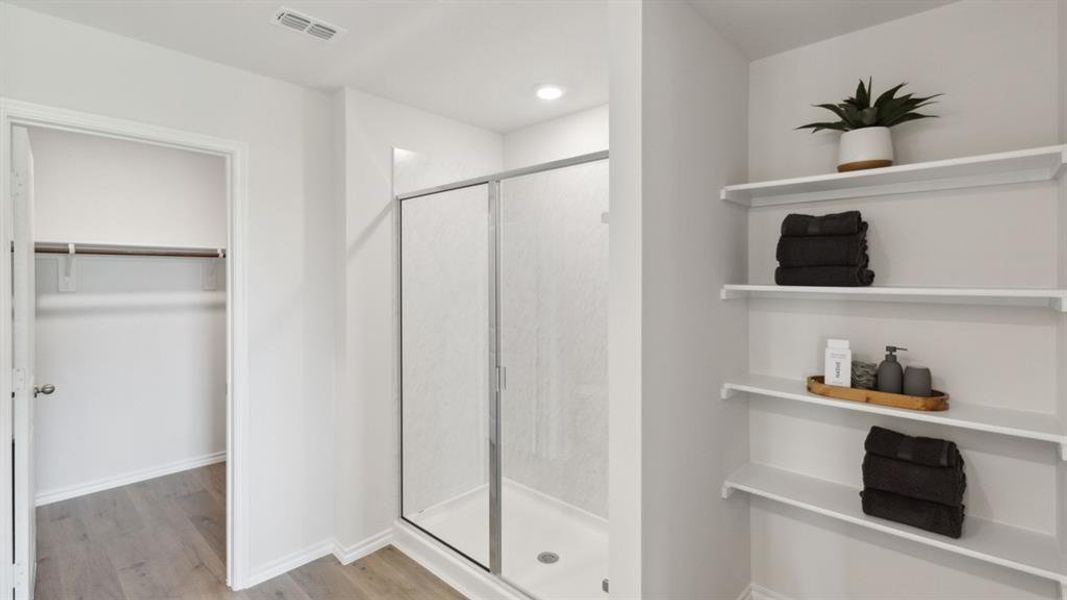 Bathroom with a walk in closet, a shower stall, and light wood finished floors