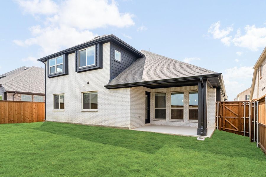 Two-story home with white brick exterior, covered patio, and fenced backyard with green lawn