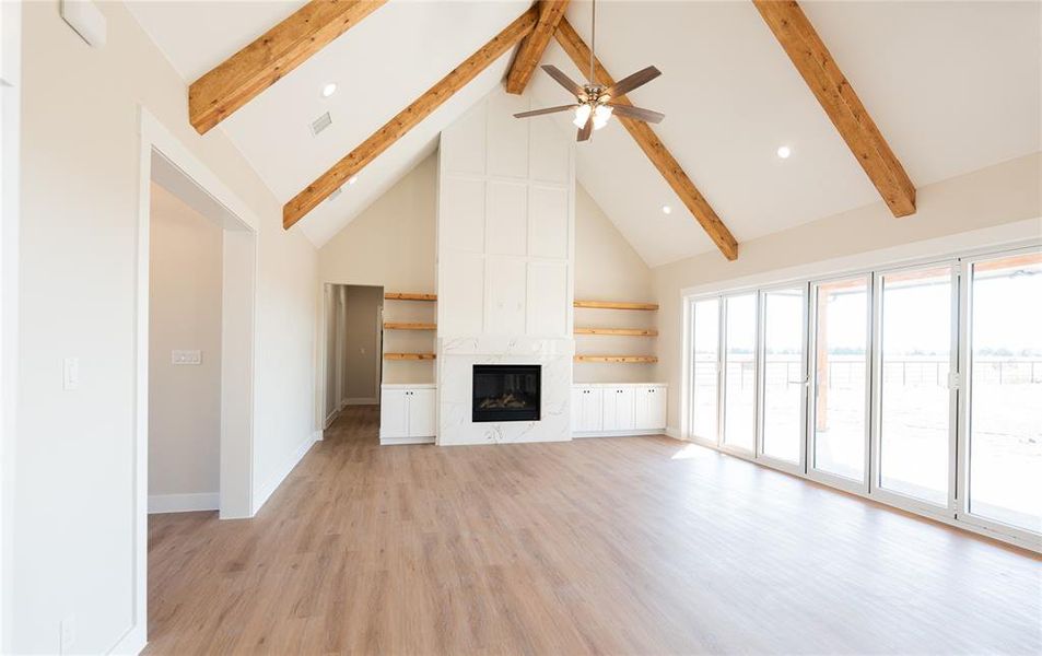 Unfurnished living room featuring high vaulted ceiling, light wood-style flooring, a premium fireplace, a ceiling fan, and beam ceiling