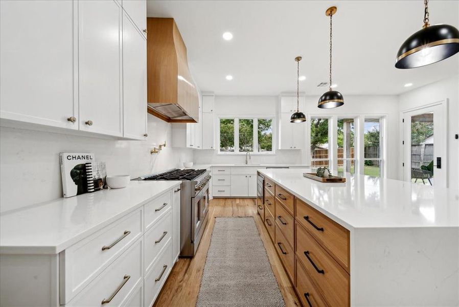 Kitchen with double oven range, premium range hood, light hardwood floors, and white cabinets