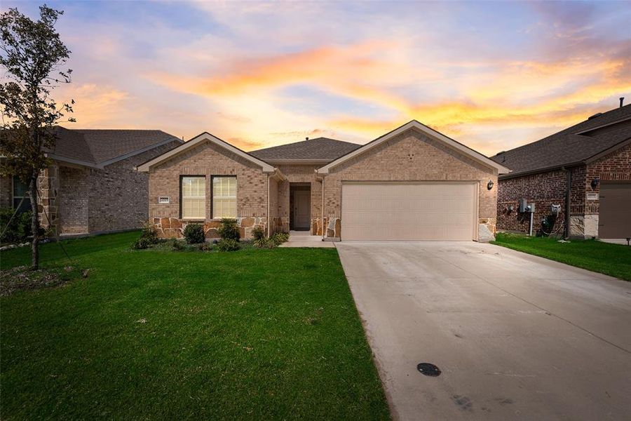 Ranch-style house featuring brick siding, roof with shingles, driveway, a garage, and stone siding Ranch-style house featuring brick siding, roof with shingles, driveway, a garage, and stone siding