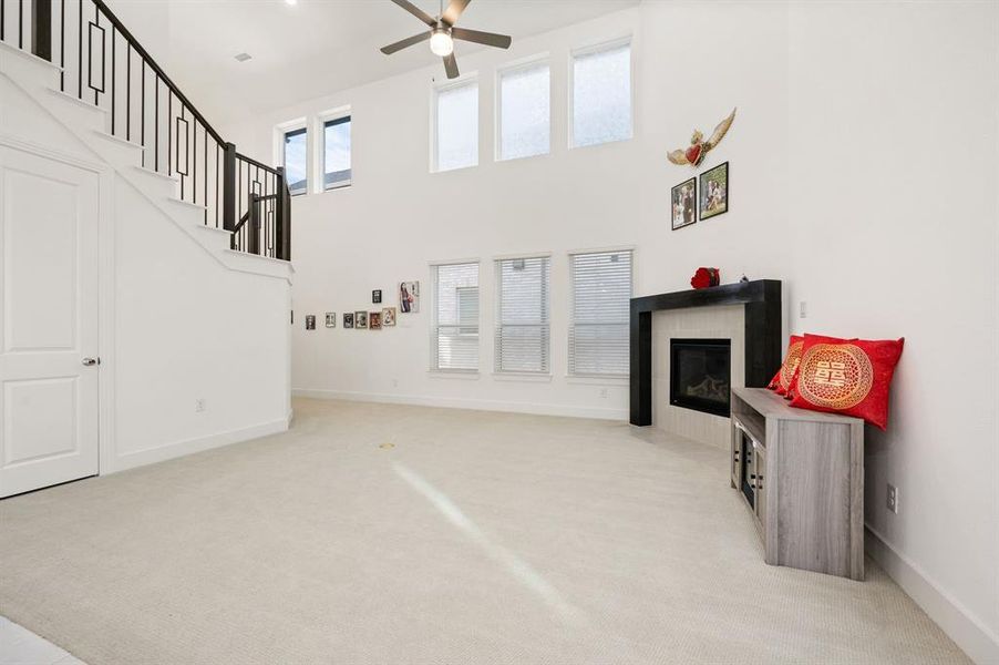 Unfurnished living room featuring light carpet, a tile fireplace, stairs, a towering ceiling, and ceiling fan