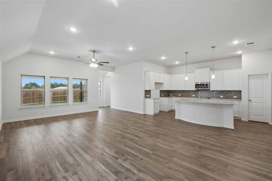 Kitchen featuring decorative backsplash, dark wood-style flooring, open floor plan, stainless steel microwave, and white cabinets Kitchen featuring decorative backsplash, dark wood-style flooring, open floor plan, stainless steel microwave, and white cabinets