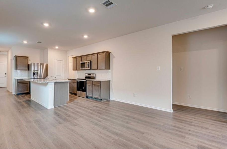 Open-concept kitchen featuring an island with a breakfast bar, stainless steel appliances, dark wood-finish cabinetry, light-colored countertops, and wood-finish flooring Open-concept kitchen featuring an island with a breakfast bar, stainless steel appliances, dark wood-finish cabinetry, light-colored countertops, and wood-finish flooring