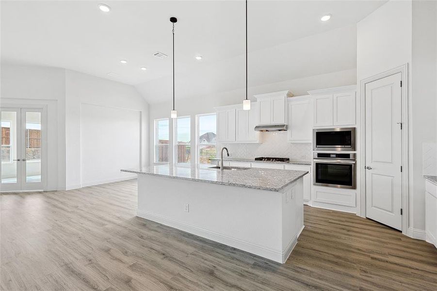 Kitchen featuring vaulted ceiling, light stone counters, white cabinets, french doors, and stainless steel appliances
