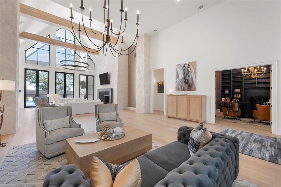 Living room with a chandelier, a desk, wood finished floors, a towering ceiling, and a fireplace