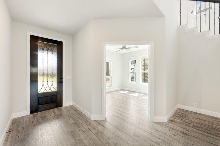 Entryway with dark wood glass-panel front door, light hardwood floors, and staircase with metal balusters