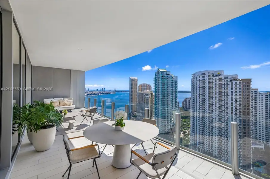 Expansive covered balcony with large-format tile flooring and a glass railing, showcasing a panorama of the surrounding urban skyline and water