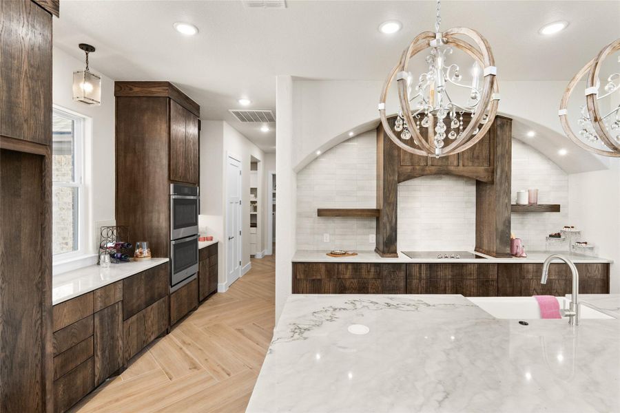 Kitchen featuring light stone countertops, dark brown cabinetry, a chandelier, recessed lighting, and pendant lighting