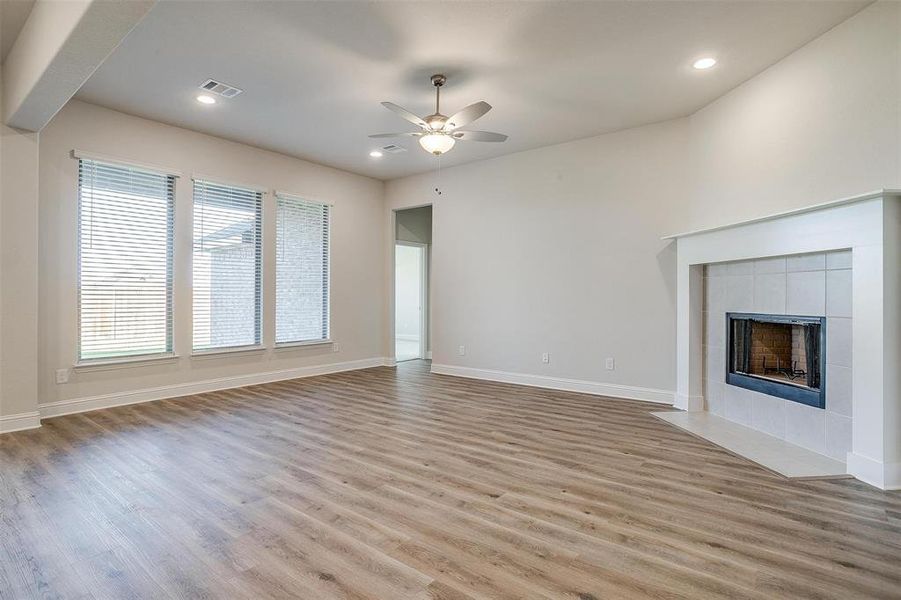 Unfurnished living room featuring a tile fireplace, light wood-type flooring, and ceiling fan