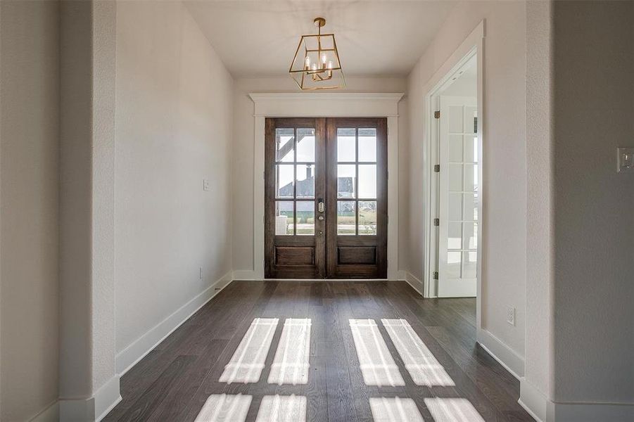 Entryway with an inviting chandelier, french doors, and dark wood-type flooring