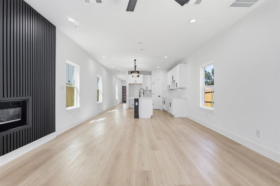 Open-concept living area featuring light wood-finish flooring, recessed lighting, and a modern fireplace with a black slatted accent wall Open-concept living area featuring light wood-finish flooring, recessed lighting, and a modern fireplace with a black slatted accent wall