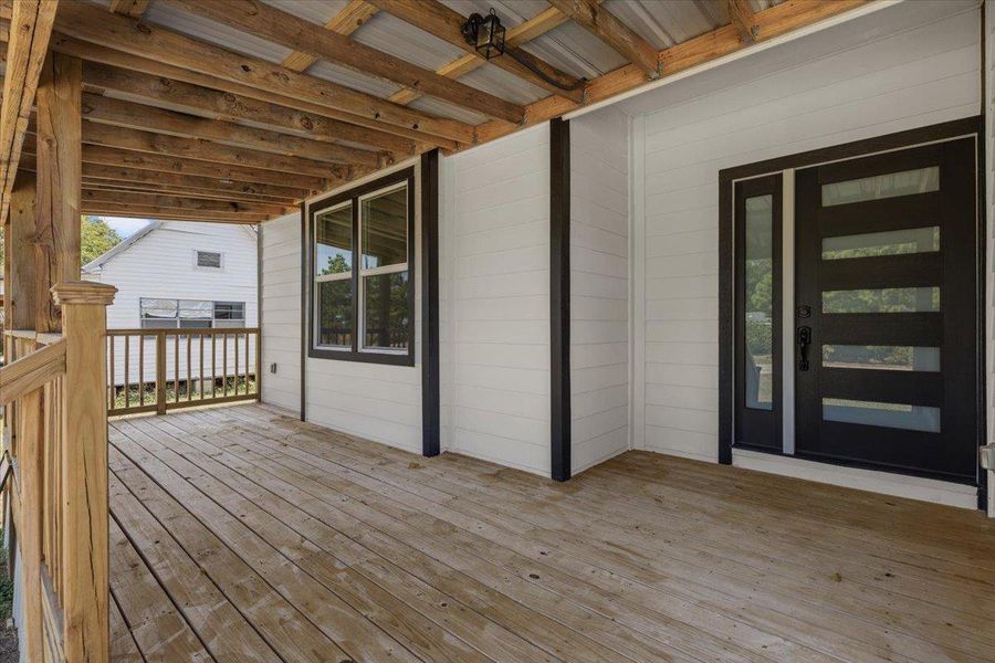 Natural wood decking and exposed ceiling beams frame a modern entryway with horizontal glass panels. Natural wood decking and exposed ceiling beams frame a modern entryway with horizontal glass panels.