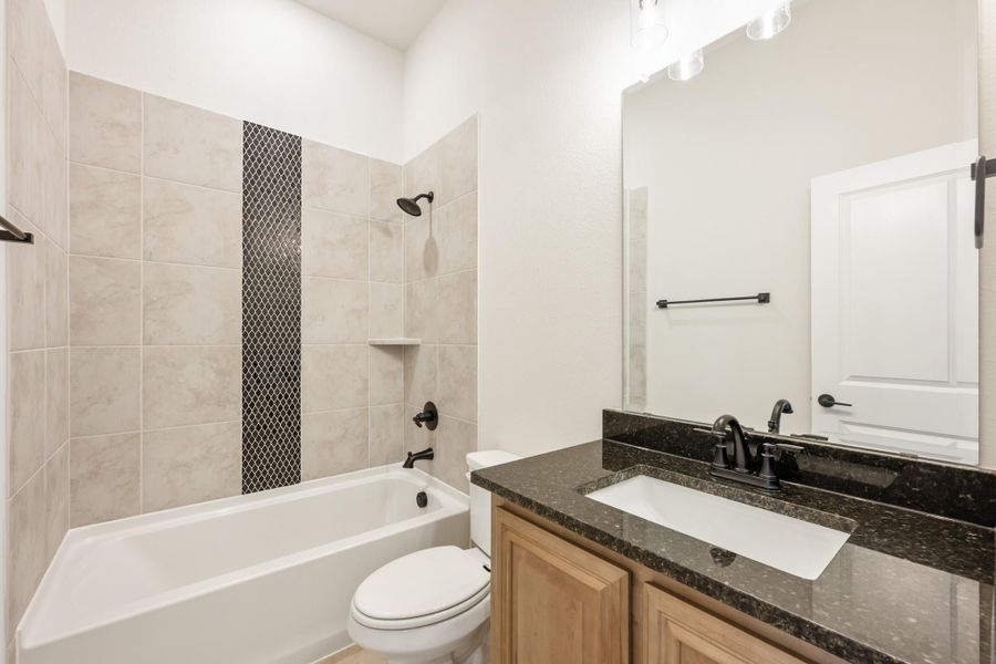 Bathroom with tiled tub-shower combo, dark granite vanity, wood cabinets, and black fixtures Bathroom with tiled tub-shower combo, dark granite vanity, wood cabinets, and black fixtures