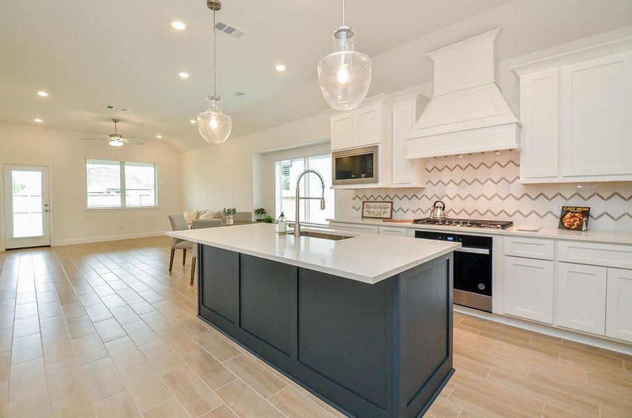 A spacious, modern kitchen and dining area featuring a large island with a sleek countertop, white cabinetry, and a stylish chevron backsplash. The open floor plan allows for ample natural light, enhanced by pendant lighting and recessed ceiling lights. Perfect for entertaining and everyday living.