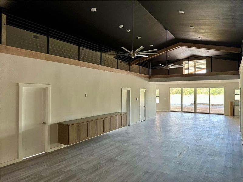 Empty room with wood-type flooring, ceiling fan, and high vaulted ceiling