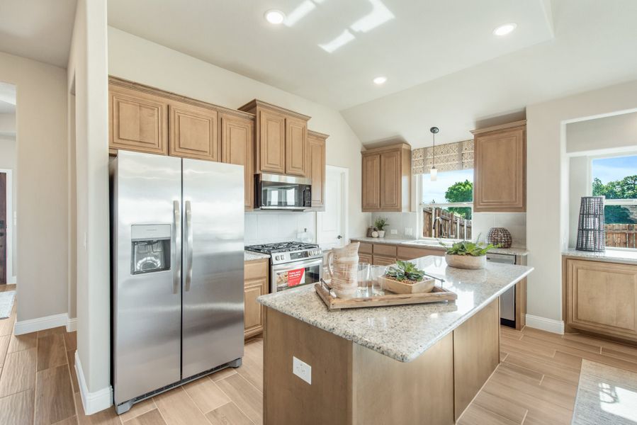 Kitchen with light wood cabinets, granite island, and stainless steel appliances on tile floors