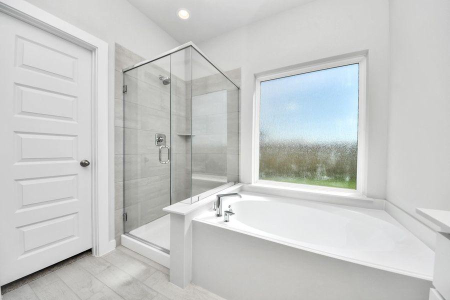 Indulge in a spa-like retreat within the confines of this primary bathroom. Delight in a spacious walk-in shower enveloped in stylish tile surround, unwind in a separate garden tub adorned with custom detailing. Sample photo of completed home with similar floor plan. Actual colors and selections may vary.