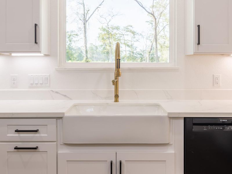 Enjoy serene outdoor views while doing dishes at the large apron-front farmhouse sink. Flanked by white shaker cabinets and framed by soft natural light, this area blends luxury with utility. Enjoy serene outdoor views while doing dishes at the large apron-front farmhouse sink. Flanked by white shaker cabinets and framed by soft natural light, this area blends luxury with utility.