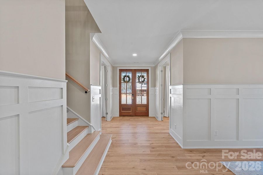 Exceptional craftsmanship on display—gorgeous floors, custom wainscoting, and elegant, solid mahogany double doors create a striking entry.