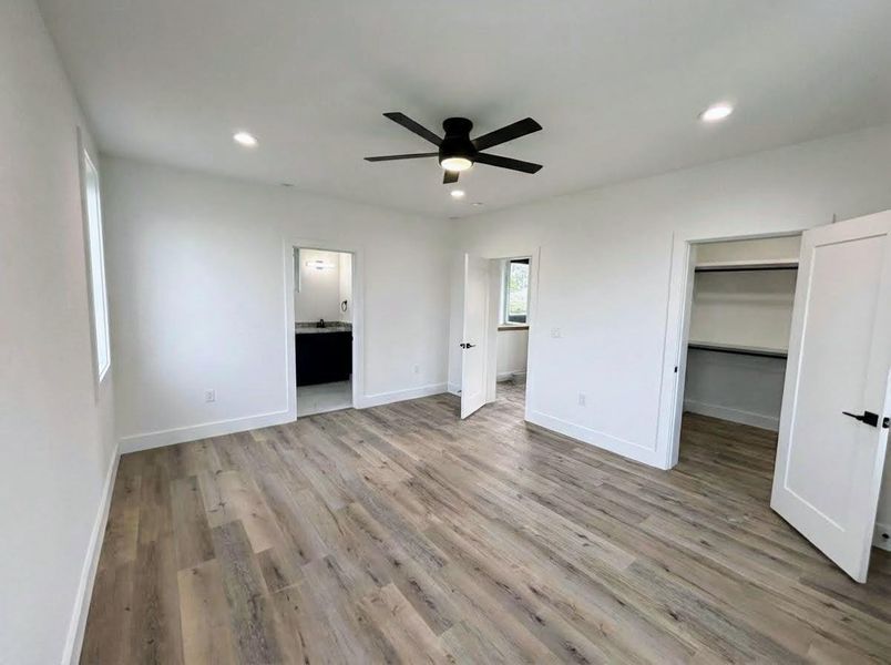 Unfurnished bedroom with light wood-style flooring, a walk in closet, a ceiling fan, recessed lighting, and ensuite bathroom