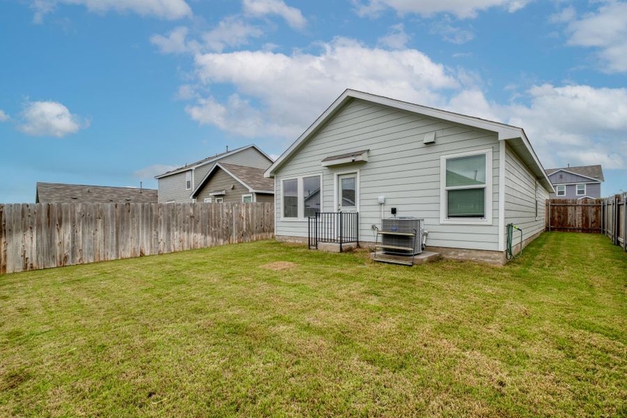 Expansive grassy backyard featuring a light gray siding exterior, multiple windows, a rear entry door, and a full perimeter wood fence