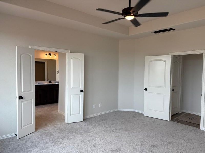 Carpeted interior room with a tray ceiling and a ceiling fan with integrated lighting