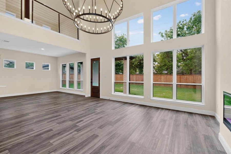 Vaulted living space featuring an oversized chandelier, a two-story window array overlooking a fenced backyard, and wood-finish flooring