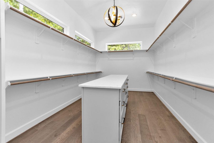 This expansive walk-in closet delivers a true wow factor with a statement chandelier, custom built-ins, double hanging rods, a center island with storage and transom windows that fill the space with natural light.